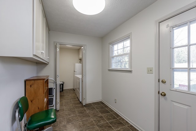 interior space with a textured ceiling, cabinet space, a wealth of natural light, and washer and dryer