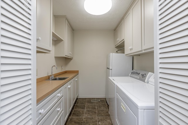 laundry room with a textured ceiling, a sink, baseboards, washer and dryer, and cabinet space