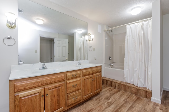 full bath featuring a textured ceiling, visible vents, a sink, and wood finished floors