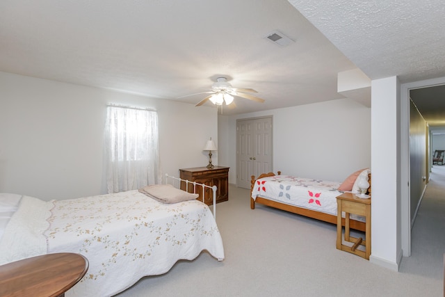 carpeted bedroom featuring a ceiling fan, a closet, visible vents, and a textured ceiling