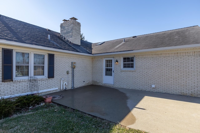 exterior space featuring a patio area, brick siding, a chimney, and roof with shingles