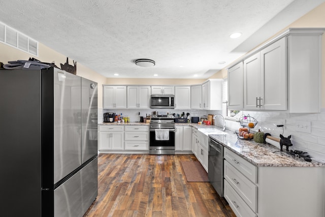 kitchen with visible vents, decorative backsplash, dark wood finished floors, stainless steel appliances, and a sink