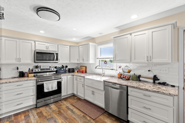 kitchen with decorative backsplash, appliances with stainless steel finishes, dark wood-type flooring, white cabinetry, and a sink