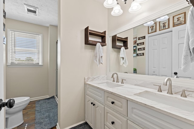 full bath featuring a sink, a textured ceiling, toilet, and double vanity