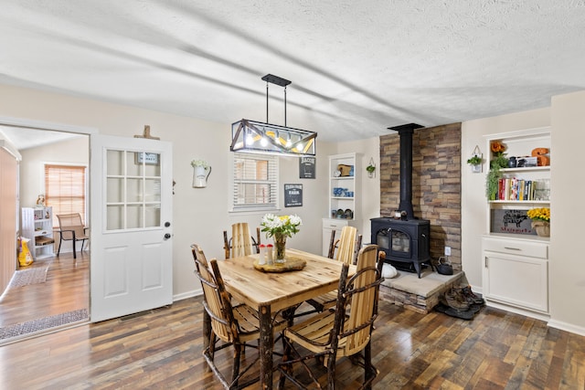 dining room featuring a textured ceiling, dark wood finished floors, a wood stove, and baseboards