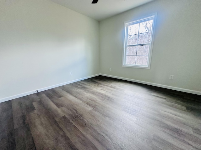 empty room with dark wood finished floors, a ceiling fan, and baseboards