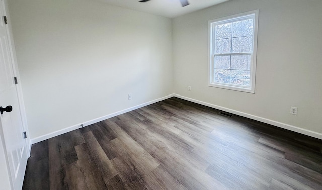 empty room with dark wood-type flooring, a ceiling fan, visible vents, and baseboards