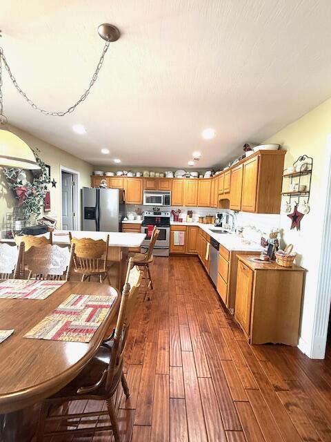 kitchen featuring a sink, light countertops, appliances with stainless steel finishes, brown cabinetry, and dark wood finished floors