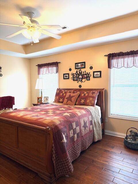 bedroom featuring a ceiling fan, a tray ceiling, wood-type flooring, and baseboards