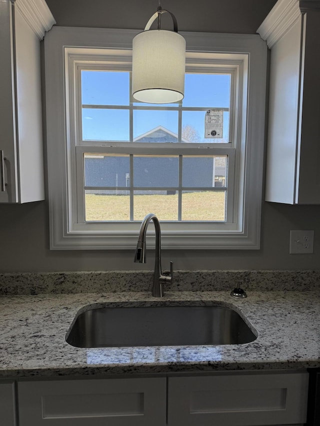 kitchen featuring a wealth of natural light, white cabinets, a sink, and light stone countertops