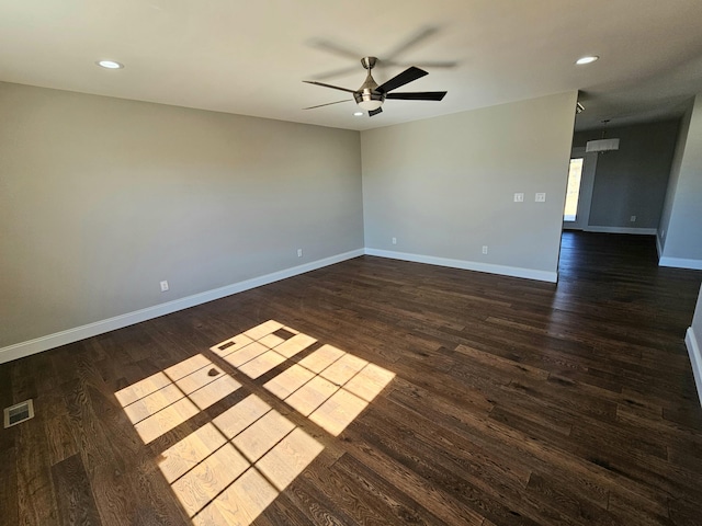 empty room with ceiling fan, dark wood finished floors, visible vents, and baseboards