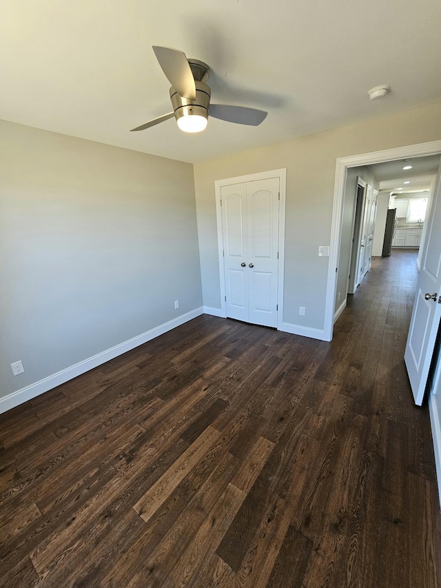 unfurnished bedroom with dark wood-style floors, a closet, a ceiling fan, and baseboards