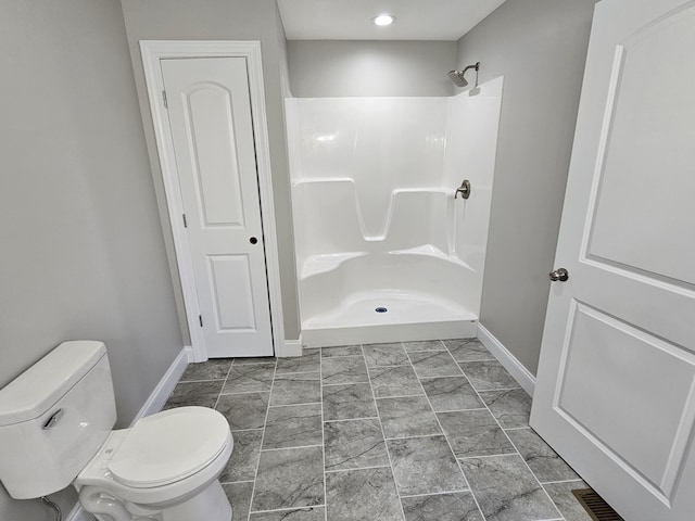 bathroom with a shower stall, toilet, and baseboards