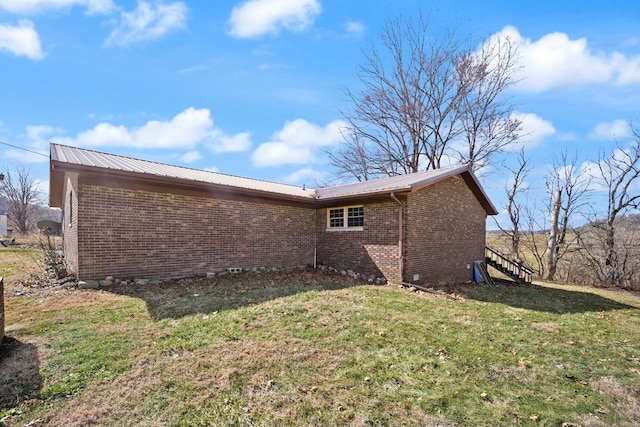 view of side of property featuring metal roof, brick siding, a lawn, and stairway