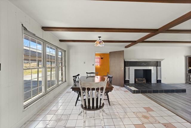 dining room featuring a fireplace with raised hearth, light tile patterned floors, and beam ceiling