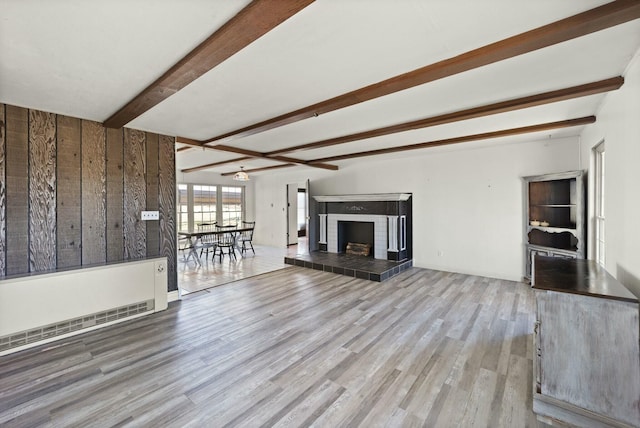 unfurnished living room with beamed ceiling, a tiled fireplace, and wood finished floors