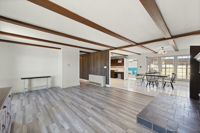 unfurnished living room featuring wooden walls, baseboards, beamed ceiling, wood finished floors, and heating unit