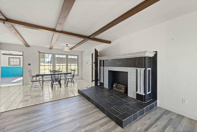 living area with a tile fireplace, wood finished floors, and beam ceiling