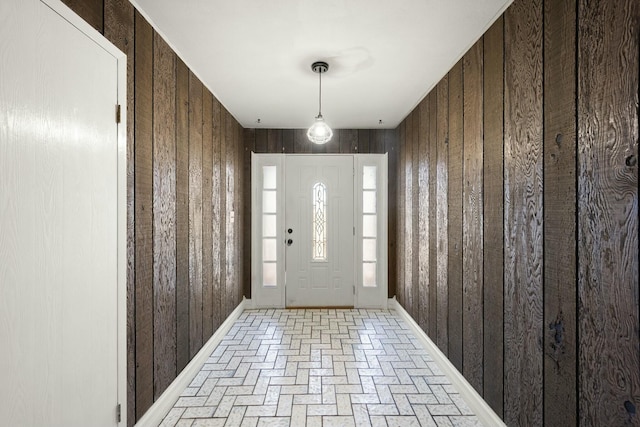 foyer with brick floor, wood walls, and baseboards