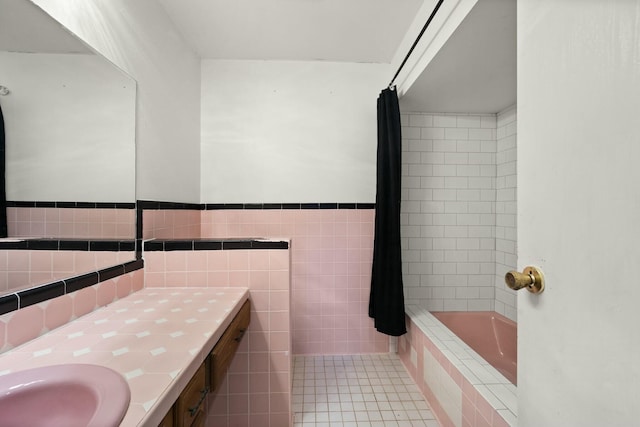 full bath featuring tile patterned flooring, tiled shower / bath combo, vanity, tile walls, and wainscoting