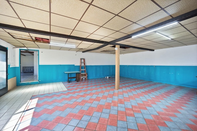 finished below grade area with a wainscoted wall, a drop ceiling, and tile patterned floors