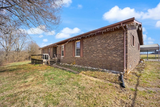 view of side of home featuring a detached carport, brick siding, a lawn, and a wooden deck