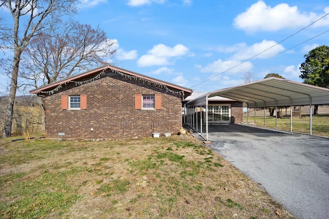 view of side of property featuring brick siding, aphalt driveway, crawl space, a yard, and a detached carport