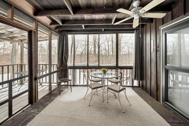 unfurnished sunroom featuring wooden ceiling, beam ceiling, plenty of natural light, and a ceiling fan