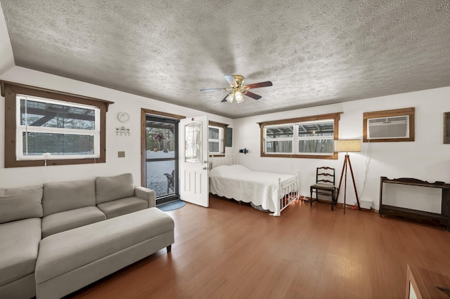 bedroom featuring access to outside, an AC wall unit, a textured ceiling, and wood finished floors