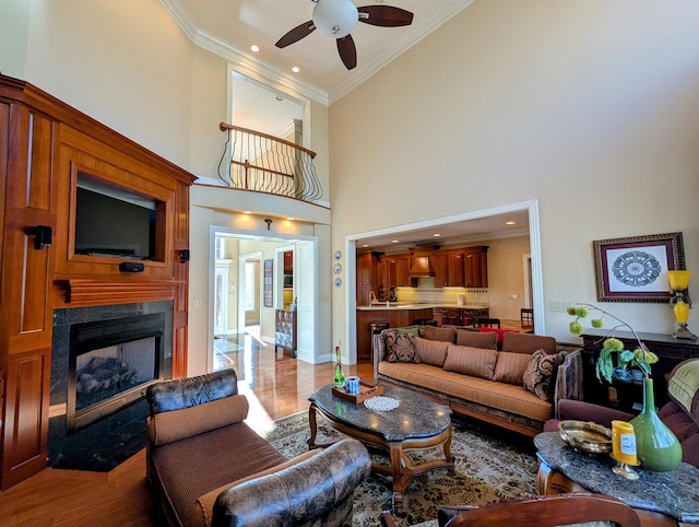 living area with a fireplace with flush hearth, ceiling fan, ornamental molding, and wood finished floors