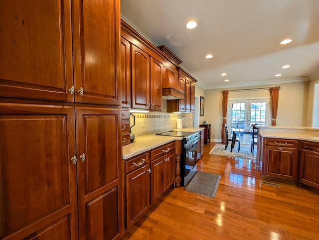 kitchen with wood finished floors, custom range hood, light countertops, electric range oven, and crown molding