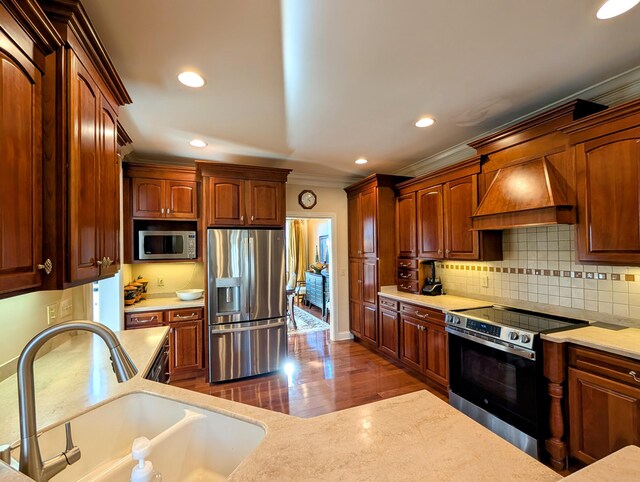 kitchen with a sink, custom range hood, appliances with stainless steel finishes, backsplash, and crown molding