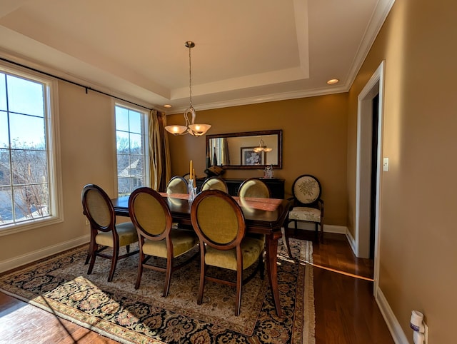 dining room with a raised ceiling, dark wood-type flooring, ornamental molding, a chandelier, and baseboards