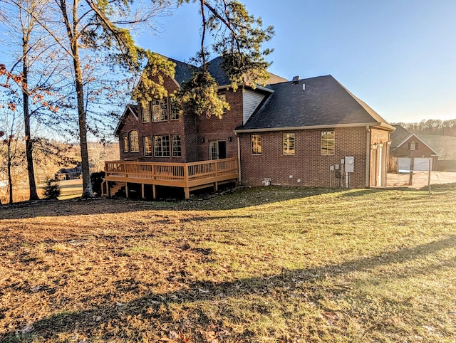 rear view of property featuring roof with shingles, brick siding, a lawn, and a wooden deck