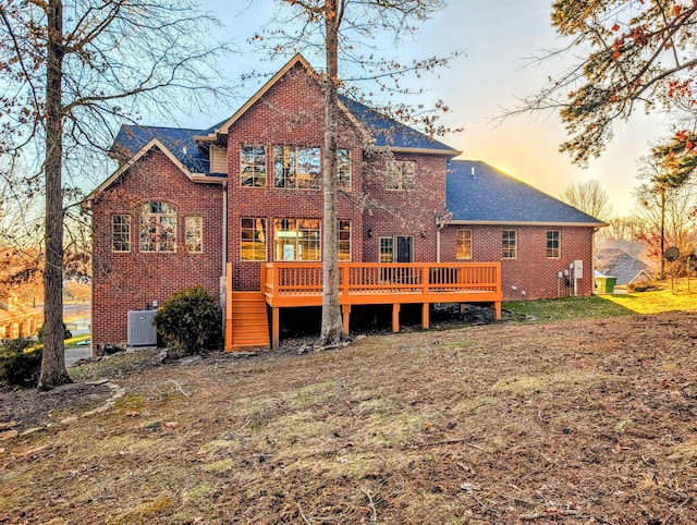 back of property at dusk with brick siding, a wooden deck, and central air condition unit