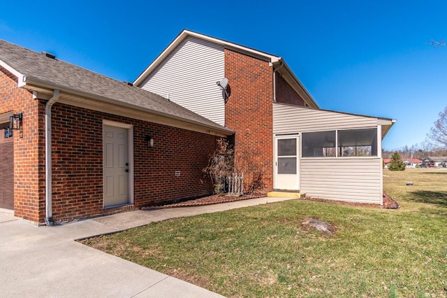 back of property with an attached garage, brick siding, a sunroom, and a yard