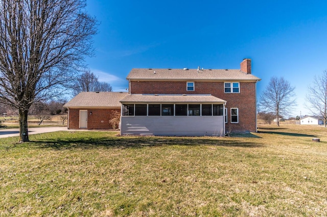 rear view of house with a sunroom, brick siding, a lawn, and a chimney