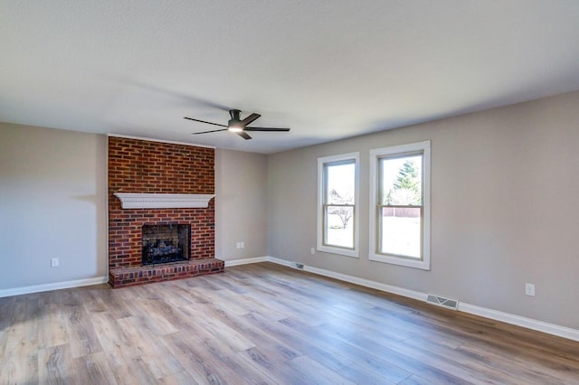 unfurnished living room featuring visible vents, a brick fireplace, ceiling fan, wood finished floors, and baseboards