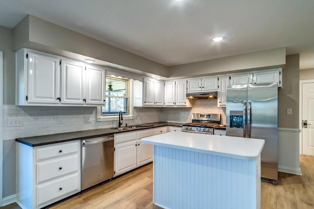 kitchen featuring light wood finished floors, stainless steel appliances, white cabinets, a sink, and under cabinet range hood