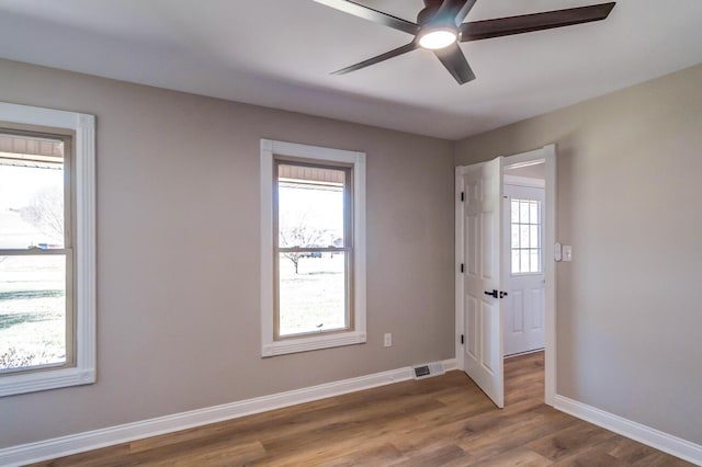 spare room featuring plenty of natural light, wood finished floors, a ceiling fan, and baseboards