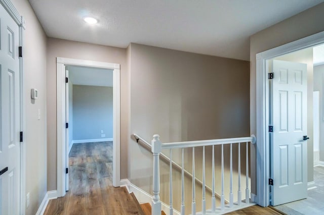 hall with wood finished floors, an upstairs landing, and baseboards