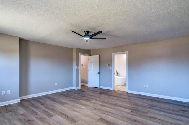 unfurnished bedroom featuring connected bathroom, a textured ceiling, baseboards, and wood finished floors