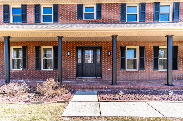 doorway to property with a porch and brick siding