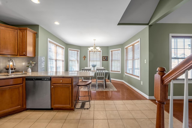 kitchen featuring tasteful backsplash, brown cabinets, dishwasher, and a sink