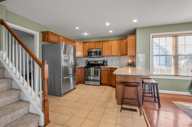 kitchen with brown cabinetry, decorative backsplash, a peninsula, stainless steel appliances, and a sink