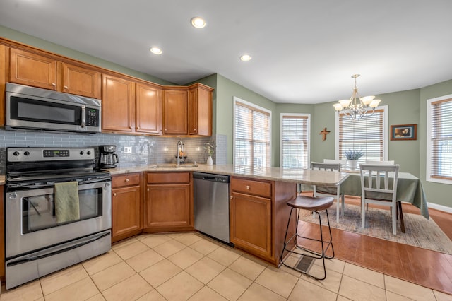 kitchen featuring brown cabinets, stainless steel appliances, light tile patterned flooring, a sink, and a peninsula