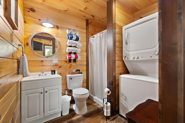 full bath with wood walls, toilet, stacked washer and clothes dryer, wood finished floors, and vanity