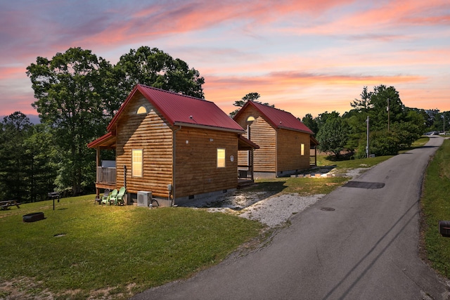 property exterior at dusk with aphalt driveway, a yard, metal roof, and crawl space