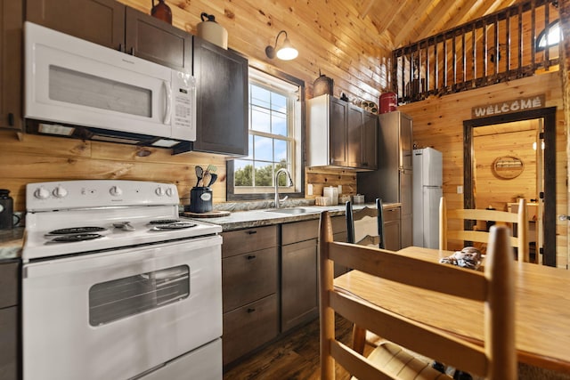 kitchen with a sink, white appliances, lofted ceiling, and wood walls