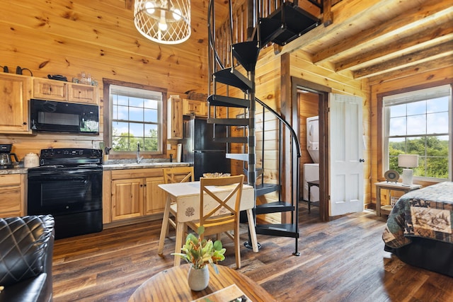 kitchen with wooden walls, stacked washer and dryer, dark wood-style floors, black appliances, and a sink